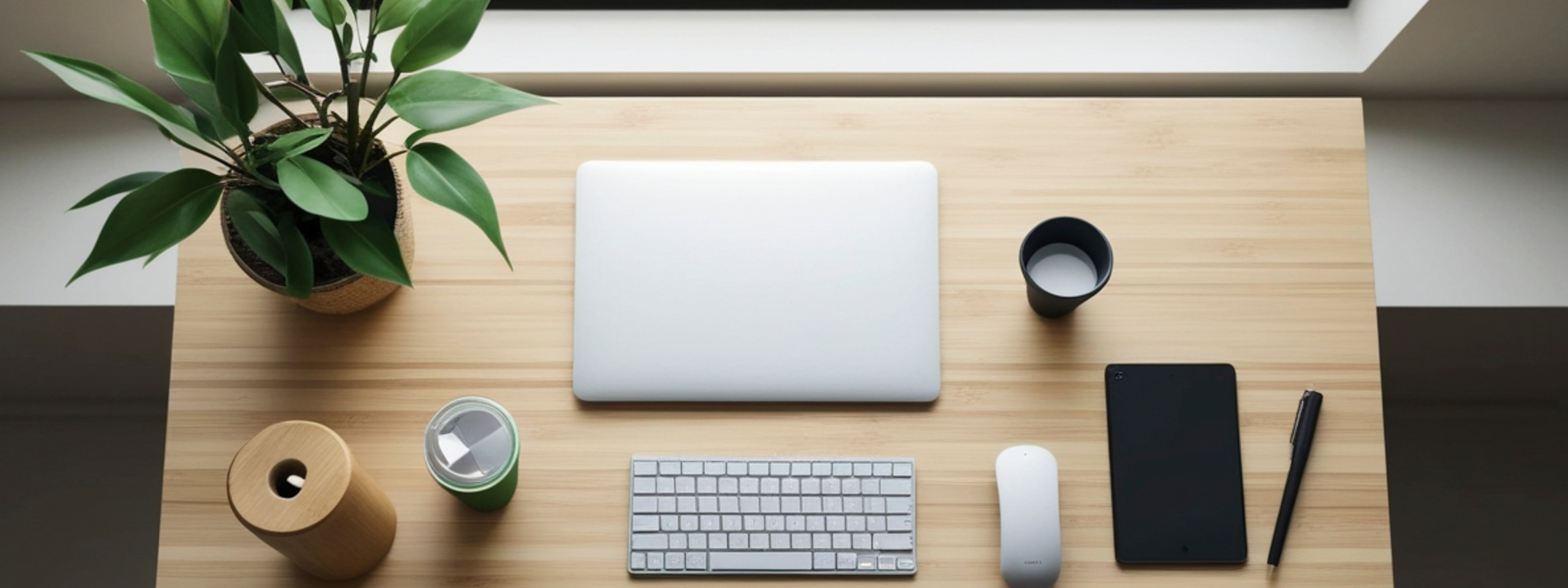 Minimalist desk setup with laptop, keyboard, mouse, and office items on a wooden surface.