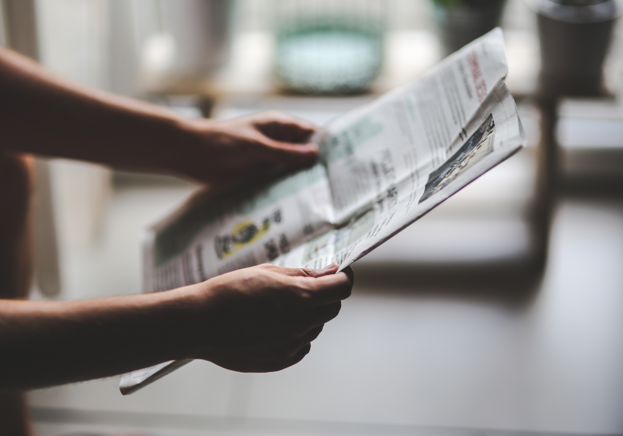 Person holding a newspaper with a blurred indoor background