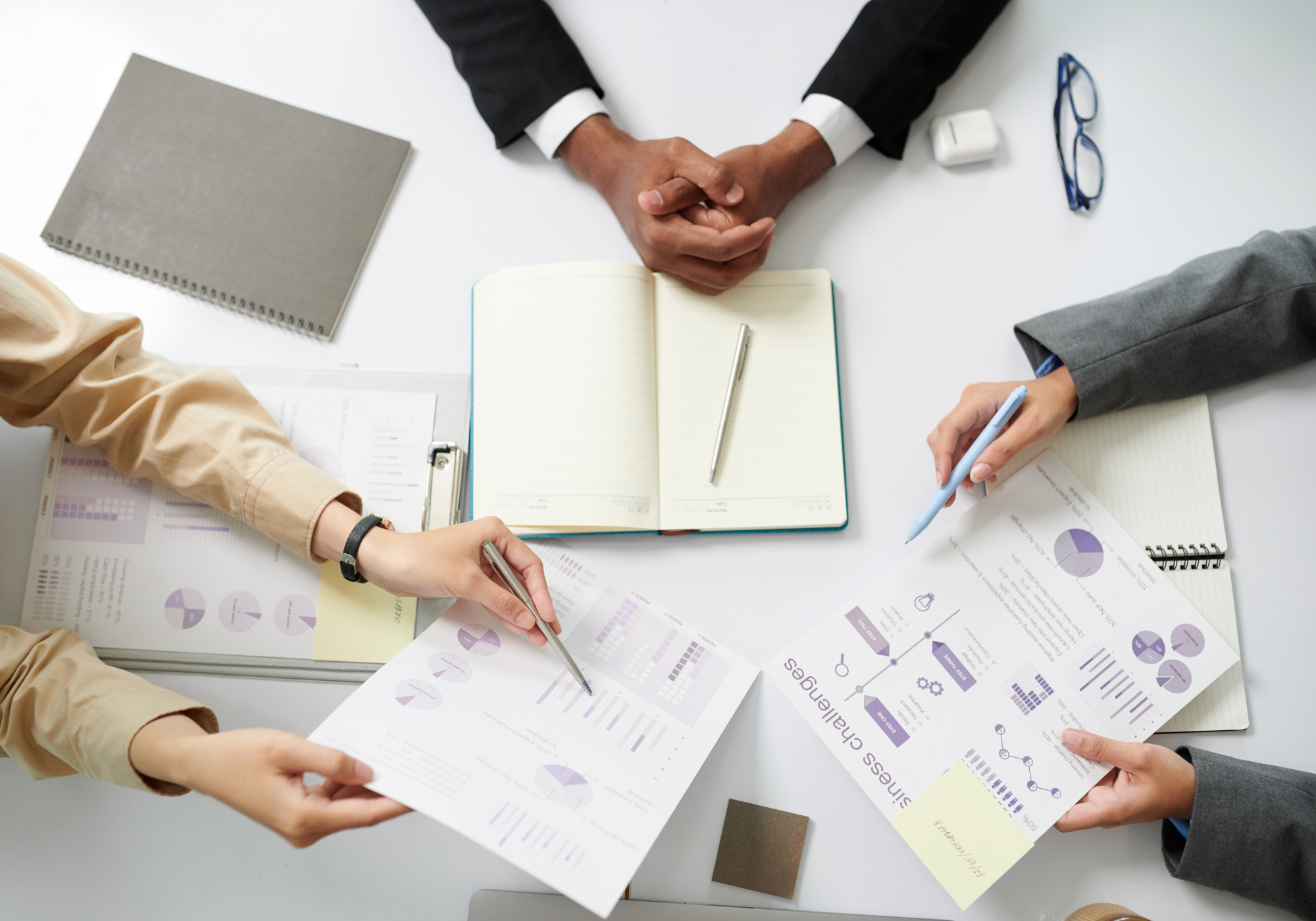 Four people working together at a table with documents and notebooks.