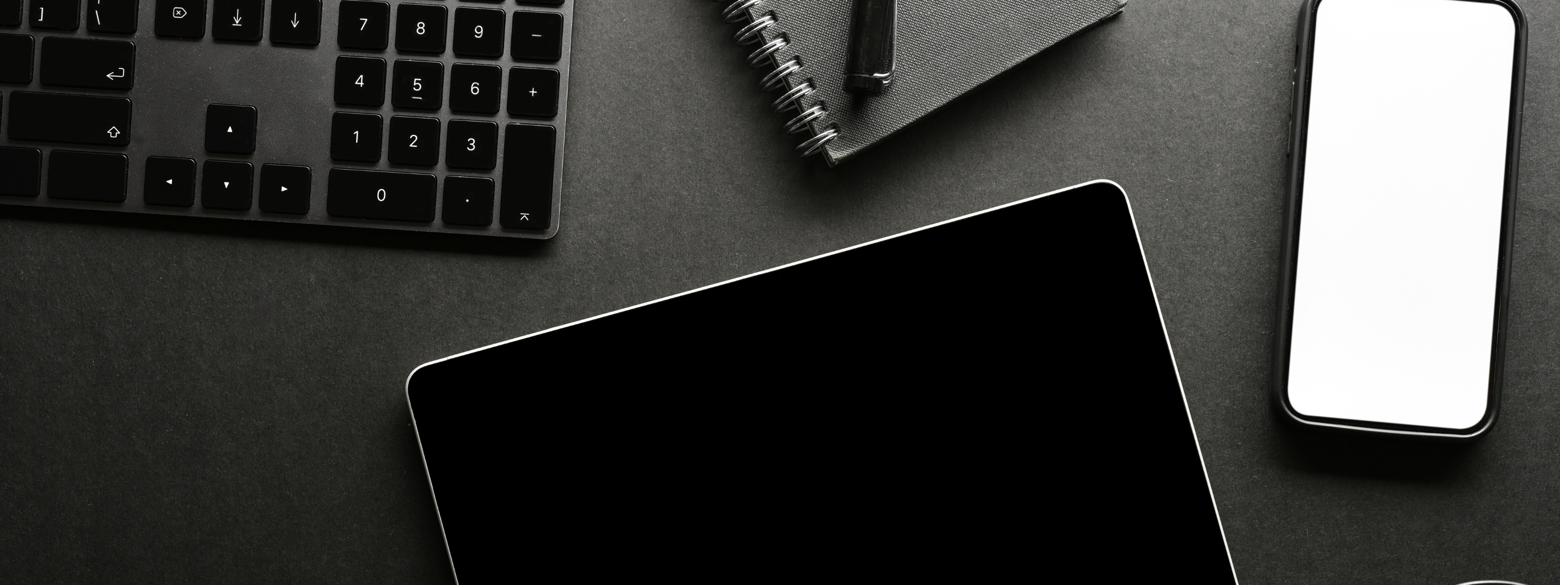 Black and white office desk setup with tablet, smartphone, and keyboard.